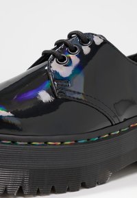 Chaussure en cuir verni noir avec lacets noirs, semelle épaisse à rainures et surpiqûres multicolores le long du bord de la semelle.