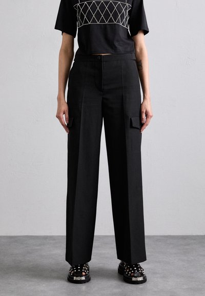 Pantaloni cargo negri cu un design larg, având buzunare frontale și o textură netedă, asortați cu un top scurt negru cu modele în formă de diamant.