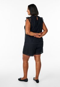 Czarny koronkowy strój z bezrękawnikem i krótkimi spodniami, z dekoltem w kształcie łezki, falbaniastymi brzegami i wygodnymi czarnymi baletkami.