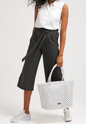 Gestreepte zwart-witte culotte broek, wit mouwloos shirt en een witte geweven draagtas met een textuur en grijze accenten en handvatten.