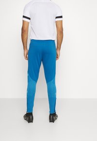 Blauwe sportbroek met een gestructureerd ontwerp en een geometrisch patroon. Gemaakt van rekbaar materiaal, ze hebben een aansluitende pasvorm en ritsen bij de enkels.