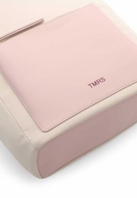 Borsa beige chiara con una tasca rosa lucida che presenta il logo "TMRS" in rilievo. Forma rettangolare con texture liscia e morbida.