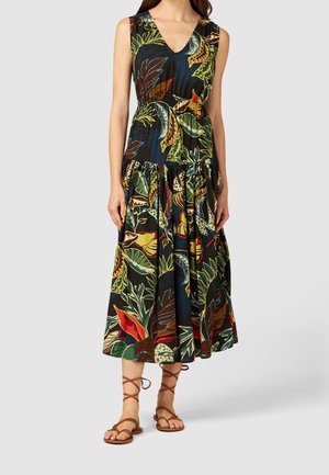 Floral-patterned maxi dress in black fabric with a V-neck, fitted bodice, and tiered skirt. Paired with brown strappy sandals.