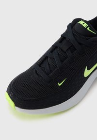 Czarny but do biegania Nike z neonowo zielonymi logo Swoosh, czarnymi sznurowadłami i białą podeszwą na jednolitym białym tle.