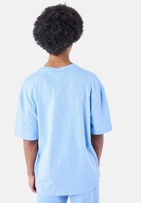 Lichtblauwe oversized t-shirt, korte mouwen, katoen materiaal, ronde hals, soepele textuur, achterkant toont een relaxte pasvorm en details van de schoudernaden.