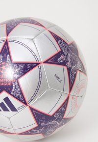 Hõbedane jalgpall suuruses 5, millel on lilla ja roosa tähdesign, ning trükitud graafika, sealhulgas dinosauruse ja UEFA Meistrite Liiga logo.