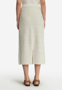 Knelång krämfärgad vävd kjol med slits bak, texturerad tyg och hög midja. Matchas med bruna sandaler.