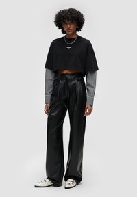 T-shirt cropped nera sopra una maglietta a maniche lunghe bianca e nera a strisce, abbinato a pantaloni in pelle nera a vita alta e scarpe bianche.