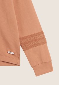 Camicia a maniche lunghe color pescato con dettaglio a maglia testurizzata sui polsini, caratterizzata da una piccola etichetta "FREDDY" sull'orlo. Materiale in cotone liscio.