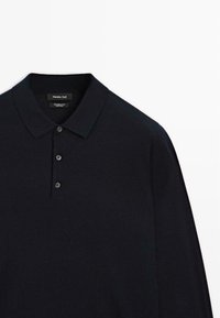 Marineblauer, gestrickter Wollpolo mit strukturiertem Kragen, Knopfleiste mit drei Knöpfen und langen Ärmeln. Weiche Textur und minimalistisches Design.