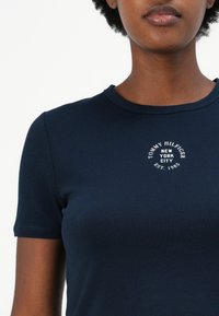 T-shirt bleu marine à manches courtes avec un col rond, arborant un logo brodé blanc qui indique "TOMMY HILFIGER NEW YORK CITY EST. 1985."