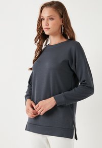 Felpa grigio scuro a maniche lunghe con scollo rotondo, spacchi laterali e una texture liscia. Progettata con una vestibilità comoda.