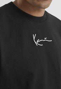 Sweatshirt en coton noir avec col ras du cou et col en rib ribé, doté de détails brodés en blanc sur la poitrine.