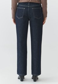 Jeans de mezclilla de color azul oscuro con corte recto, que presentan dos bolsillos traseros y costuras en contraste, combinados con botas de tacón negras.