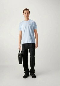 Camiseta a rayas de color azul claro en algodón, combinada con pantalones negros. El modelo lleva una bolsa negra y calza zapatos negros. Diseño sencillo, ajuste casual.