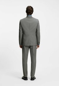 Grå skræddersyet jakkesæt med slank pasform, der har en glat tekstur, hakklap og diskret ternet mønster. Båret med sorte sko.