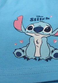 T-shirt en coton bleu clair arborant un graphique d'un alien cartoon avec de grandes oreilles et des yeux ronds, entouré de petits cœurs roses.