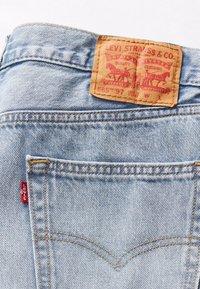 Poche arrière d'un jean en denim bleu clair avec surpiqûres orange, étiquette rouge Levi's et étiquette de marque en cuir marron Levi Strauss & Co. au-dessus de la poche.