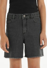 Černé džínové šortky s roztrhaným lemem, designem s pěti kapsami, stříbrným knoflíkem a mírně vybledlou texturou. Vhodné pro běžné nošení.