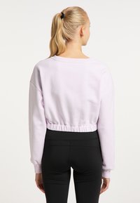 Világoslila, cropped fazonú pulóver hosszú ujjal, elasztikus derékbőséggel és laza szabással, fekete, testhezálló leggingssel párosítva.