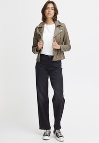Olive green leather motorcycle jacket with zipper details, white t-shirt, black wide-leg pants, and black sneakers with white soles.