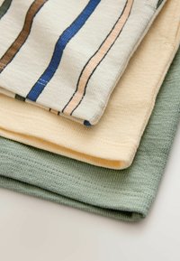 Drie handdoeken met textuur opgestapeld: bovenste is crèmekleurig met bruine, blauwe en roze strepen; middelste is effen lichtgeel; onderste is effen saliegroen.