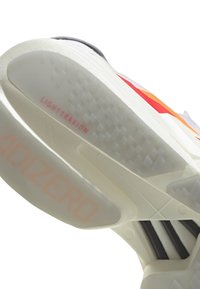Suela de una zapatilla deportiva blanca con suela de goma translúcida, marca LightTraxion y Adizero visibles, y acentos superiores en naranja y rojo.