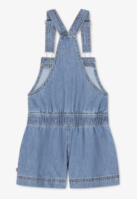 Ολόσωμη φόρμα από τζιν σε ανοιχτό μπλε χρώμα με ρυθμιζόμενες τιράντες, ελαστική μέση και φαρδιά σορτς. Διαθέτει ραμμένες λεπτομέρειες και πλαϊνές τσέπες.