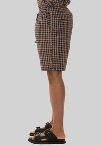 Shorts marroni a fantasia con un motivo a pois neri, dotati di una cintura elastica e tasche laterali, abbinati a sandali neri.