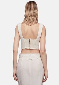 Top bianco cropped con spalline larghe, schiena texturizzata e zip nascosta. Indossato con una gonna alta coordinata di colore chiaro.