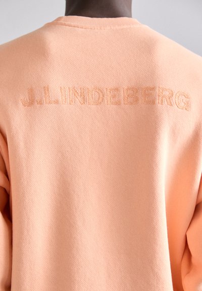 Sweatshirt de culoare piersică, realizat dintr-un material moale. Prezintă un guler rotund și text brodat "J. LINDEBERG" pe spate.