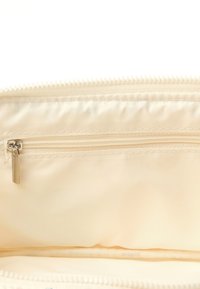 Kremowa wewnętrzna kieszeń z zamkiem błyskawicznym na górze, z mniejszą kieszonką na zamek. Gładka tekstura materiału, starannie obszyte krawędzie.