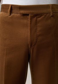 Bruine corduroy broek met een platte voorkant, riemlussen en zijzakken. Gestructureerde stof met subtiele ribbels. Geen zichtbare versieringen.