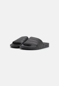 Black slide sandals made of textured rubber, featuring three horizontal stripes on the upper and a flat, simple sole.