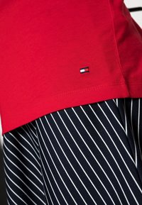 Röd bomull t-shirt med korta ärmar, prydd med en liten broderad logotyp. Kombinerad med marinblå byxor med vita vertikala ränder.