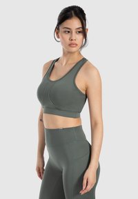 Sostén deportivo verde con diseño de espalda nadadora y detalles cosidos, combinado con leggins verdes de cintura alta que cuentan con un bolsillo lateral y una tela texturizada.