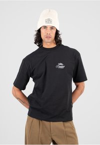 Czarna bawełniana koszulka z krótkim rękawem i okrągłym dekoltem. Posiada białe logo nadrukowane na lewej piersi. Noszona z kremową dzianinową czapką.