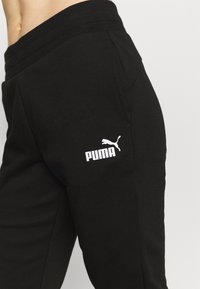 Svarta bomulls-joggingbyxor med resår i midjan, med en vit Puma-logotyp och en sidoficka. Slät textur, figurnära design.