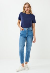 Marineblauwe T-shirt met korte mouwen gecombineerd met hoog-ubit lichte spijkerbroek en witte sneakers. Soepele stof, ontspannen pasvorm en klassieke denimstijl.