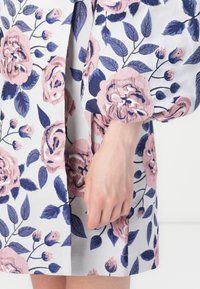 Φλοράλ φόρεμα με ανοιχτό γκρι ύφασμα και ροζ και ναυτικά μπλε σχέδια ροζών. Οι φο�υσκωτοί ώμοι και η ίσια γραμμή ενισχύουν το σχέδιο.