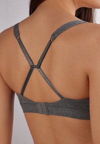 Grå sport-bh med texturerad tyg, X-back axelband, justerbar hårdvara och hakspänne vid bandet.
