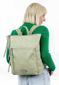 Zaino in pelle verde con doppie spalline, un manico superiore, una tasca frontale con zip e una superficie liscia. Design minimalista con accenti sottili.