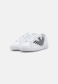 Hvite sneakers med svarte diagonale striper, rund tå, snøring, glatt syntetisk materiale og teksturert gummisåle.
