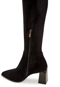 Zwarte faux suède over-de-knie laars met een puntige neus, voorzien van een zijrits en een chunky, vierkante hak voor stabiliteit.