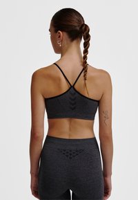 Kobieta z warkoczem w kucyku, ubrana w ciemnoszary sportowy biustonosz i legginsy, pokazująca plecy z tatuażem jaszczurki na lewym ramieniu.