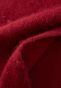 Tissu en laine rouge drapé, présentant une texture douce et duveteuse avec des nuances de rouge variées et une transition de surface lisse entre les couches.