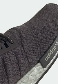 Svart stickad träningsskor med texturerad ovandel, kontrasterande gummisula och en märkt gummilapp med "adidas"-logotyp.