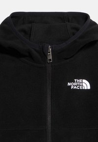 Μαύρο φλις μπουφάν με κουκούλα, κεντρικό φερμουάρ και λευκό λογότυπο «The North Face» στο αριστ ερό στήθος.