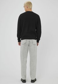 Un pull noir à côtes, un pantalon en denim gris à coupe ample et des chaussures noires. L'arrière-plan est blanc uni pour contraster.