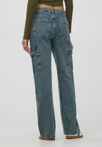 Niebieskie dżinsowe spodnie cargo o zwężanym kroju, z bocznymi kieszeniami, wysokim stanem i wyblakłą fakturą. Widoczne szwy i pięć kieszeni.